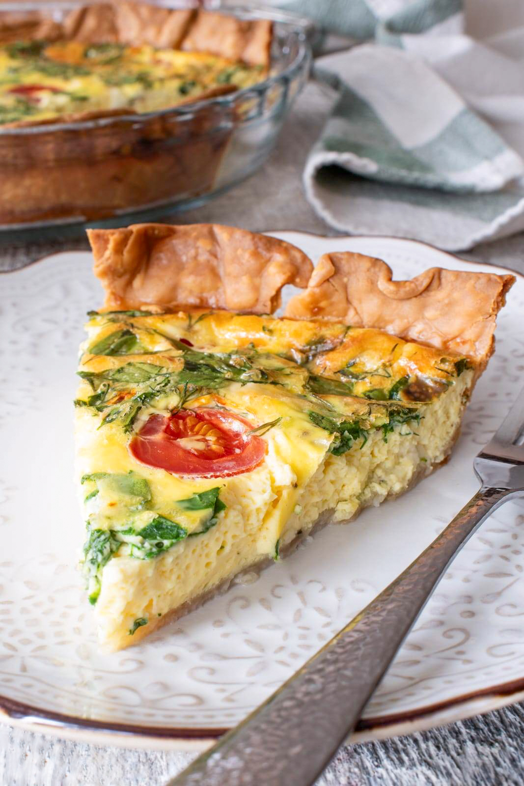triangular slice of quiche with tomatoes spinach and bacon