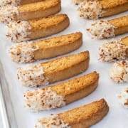 Crunchy, buttery, and full of coconut flavor, these white chocolate dipped toasted coconut biscotti are irresistible.  My whole family loves biscotti and coconut so I finally combined the two and made these deliciously crunchy toasted coconut biscotti. They were fun to make, smelled terrific while baking, and made my entire family happy. Dipping these tasty toasted coconut biscotti in coffee or tea makes them extra special. Toasted Coconut Biscotti Biscotti Ingredients: 1/2 cup unsalted butter, softened to room temperature 1/2 cup brown sugar, packed 1/2 cup white sugar 2 large eggs, room temperature 2 tsp coconut extract 3/4 tsp vanilla extract 2 1/4 cups flour 1 1/4 tsp baking powder 1/2 tsp kosher salt 1/2 cup sweetened shredded coconut Other Ingredients: 1/2 cup sweetened shredded coconut, toasted 6 oz white chocolate melting wafers 1/4 tsp coconut oil How to Make Toasted Coconut Biscotti Preheat the oven to 350 degrees. Line a baking sheet with parchment paper. Make the biscotti by using a hand mixer to beat the butter, brown sugar, and white sugar together until creamy. Beat in the eggs, one at a time, along with the coconut extract and vanilla extract until creamy and smooth. Whisk the flour, baking powder, and salt together in a small bowl. Gradually add the flour mixture to the egg mixture until just combined. Add the shredded coconut and mix until combined. Divide the dough equally in two and place each half on the baking sheet. Shape each half into an 8-9-inch long slab about 1/2-inch thick. Side Note: The dough will be sticky. Bake the biscotti for 20 minutes, or until the top and sides of the biscotti slabs are lightly browned. Remove from the oven, but do not turn off the heat.  Allow the slabs to cool for 10 minutes. Once they have cooled enough to handle, cut each slab into 1-inch wide slices then carefully place the slices back on the baking sheet cut sides upright, 1/4-inch apart. Return to the oven to bake for 8 minutes. Carefully turn the biscotti over and continue to bake for 8 minutes. The cookies will be slightly soft in the centers and harder on the edges. Side Note: They will get crunchier as they cool. Toast the coconut by placing the remaining 1/2 cup of coconut in a dry large skillet over low heat. Cook, stirring often, for 4-5 minutes, or until the coconut is golden brown and toasted. Remove from the stovetop and set aside to cool. Prepare the dipping chocolate by placing the white chocolate wafers in a glass bowl with 1/4 teaspoon of coconut oil then put into the microwave for 30 seconds. Remove and stir then place back into the microwave for 15 seconds. Remove and stir then place back into the microwave for 10 seconds. Remove and stir until completely melted. If needed, continue cooking for 10-second increments. Be careful not to overcook the white chocolate! Dip the biscotti by dipping one end of each biscotti into the melted white chocolate then immediately sprinkle the top with the toasted coconut before the white chocolate dries. Place them on a parchment-lined baking sheet. Allow them to dry completely. Store in an airtight container at room temperature for up to 2 weeks. Enjoy!   WP Recipe Maker #74759 remove Toasted Coconut Biscotti Course: Breakfast, Dessert Cuisine: Italian Prep Time: 20m Cook Time: 45m Total Time: 65m Servings: 20 biscotti +/- Author: Pam - For the Love of Cooking - Baking Sheet - Hand mixer Biscotti Ingredients: - 1/2 cup unsalted butter softened to room temperature - 1/2 cup brown sugar packed - 1/2 cup white sugar - 2 large eggs room temperature - 2 tsp coconut extract - 3/4 tsp vanilla extract - 2 1/4 cups flour - 1 1/4 tsp baking powder - 1/2 tsp kosher salt - 1/2 cup sweetened shredded coconut Other Ingredients: - 1/2 cup sweetened shredded coconut toasted - 6 oz white chocolate melting wafers - 1/4 tsp coconut oil 1) Preheat the oven to 350 degrees. Line a baking sheet with parchment paper. 2) Make the biscotti by using a hand mixer to beat the butter, brown sugar, and white sugar together until creamy. Beat in the eggs, one at a time, along with the coconut extract and vanilla extract until creamy and smooth. 3) Whisk the flour, baking powder, and salt together in a small bowl. 4) Gradually add the flour mixture to the egg mixture until just combined. 5) Add the shredded coconut and mix until combined. 6) Divide the dough equally in two and place each half on the baking sheet. Shape each half into an 8-9-inch long slab about 1/2-inch thick. Side Note: The dough will be sticky. 7) Bake the biscotti for 20 minutes, or until the top and sides of the biscotti slabs are lightly browned. Remove from the oven, but do not turn off the heat.  Allow the slabs to cool for 10 minutes. 8) Once they have cooled enough to handle, cut each slab into 1-inch wide slices then carefully place the slices back on the baking sheet cut sides upright, 1/4-inch apart. 9) Return to the oven to bake for 8 minutes. 10) Carefully turn the biscotti over and continue to bake for 8 minutes. The cookies will be slightly soft in the centers and harder on the edges. Side Note: They will get crunchier as they cool. 11) Toast the coconut by placing the remaining 1/2 cup of coconut in a dry large skillet over low heat. Cook, stirring often, for 4-5 minutes, or until the coconut is golden brown and toasted. Remove from the stovetop and set aside to cool. 12) Prepare the dipping chocolate by placing the white chocolate wafers in a glass bowl with 1/4 teaspoon of coconut oil then put into the microwave for 30 seconds. Remove and stir then place back into the microwave for 15 seconds. Remove and stir then place back into the microwave for 10 seconds. Remove and stir until completely melted. If needed, continue cooking for 10-second increments. Be careful not to overcook the white chocolate! 13) Dip the biscotti by dipping one end of each biscotti into the melted white chocolate then immediately sprinkle the top with the toasted coconut before the white chocolate dries. 14) Place them on a parchment-lined baking sheet. 15) Allow them to dry completely. Store in an airtight container at room temperature for up to 2 weeks. Enjoy!     Toasted Coconut Biscotti